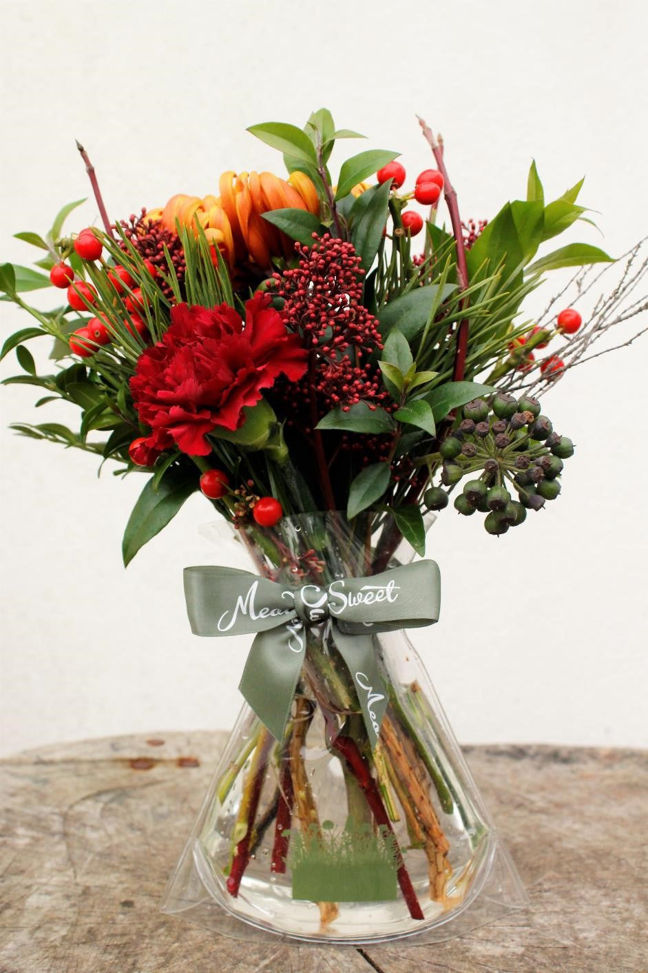 MeadowSweet seasonal posy with British pine, holly berries, box, ruscus, ivy berries, heather twigs, red dogwood and skimmia buds plus international cheer from fuego chrisanthamums and burgundy carnations.