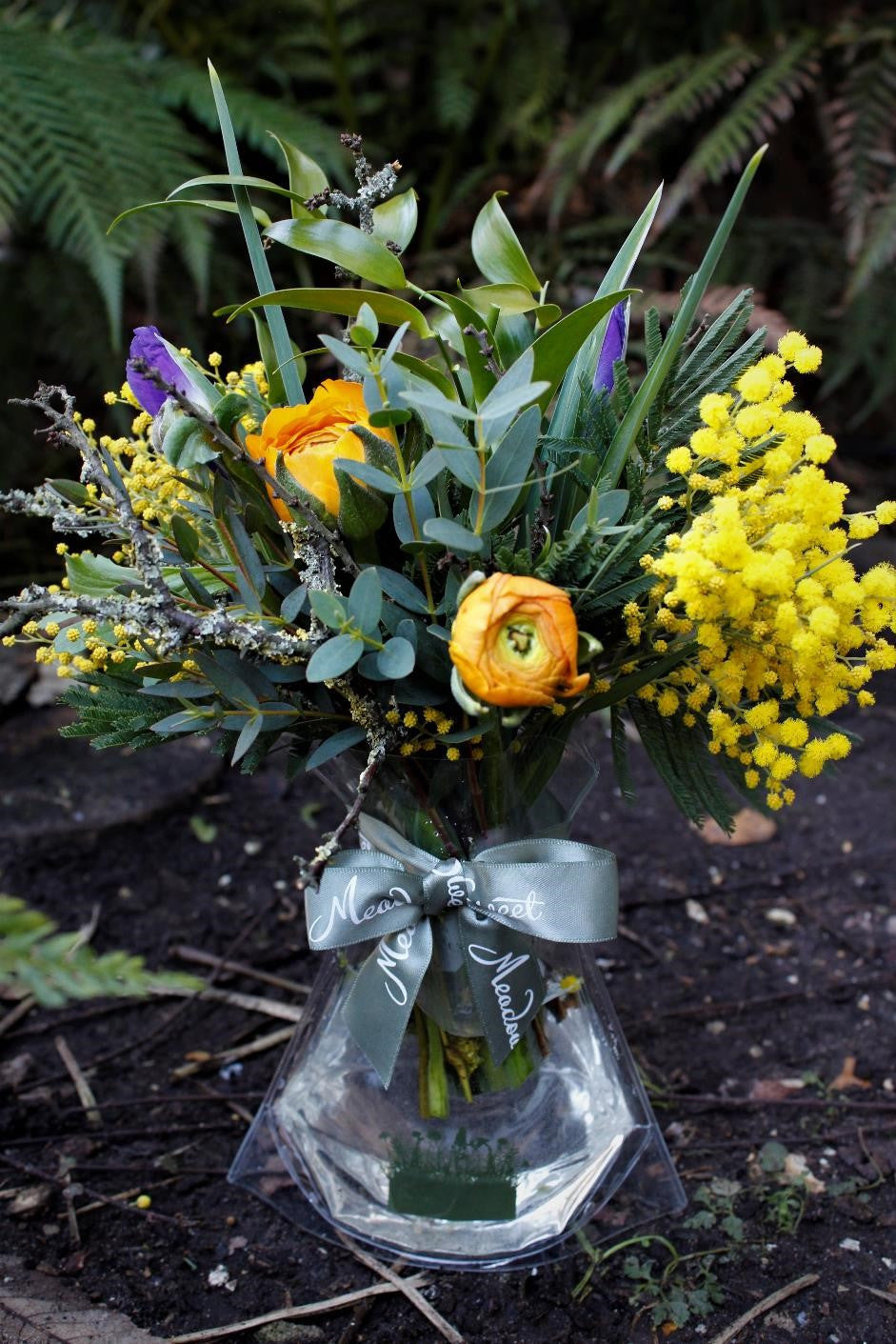 MeadowSweet seasonal posy with Orange ranunculus, blue iris and yellow mimosa with eucalyptus, ruscus and lichen-covered twigs.