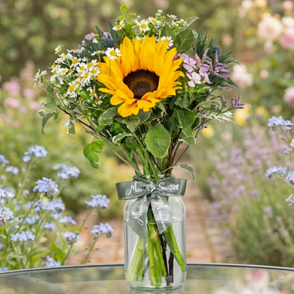 Bouquet of sunflowers and wildflowers in a glass jar with a garden background