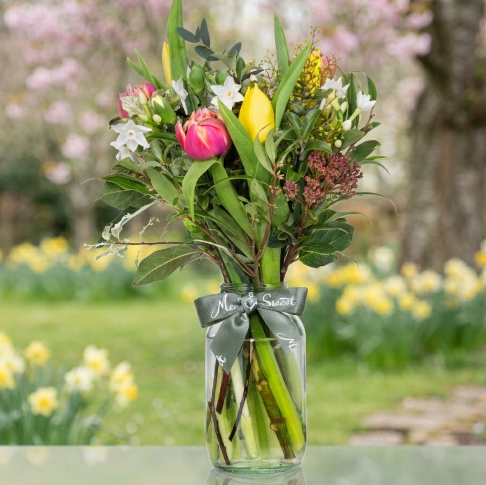 Bouquet of British grown Spring flowers in a glass vase with a garden background