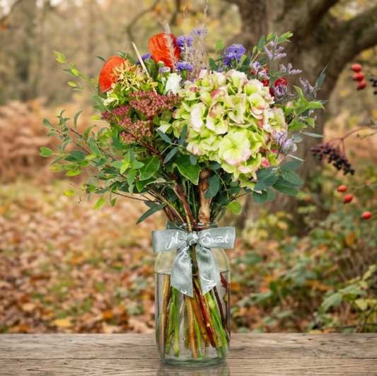 Bouquet of British grown Autumn flowers in a glass vase with a woodland background