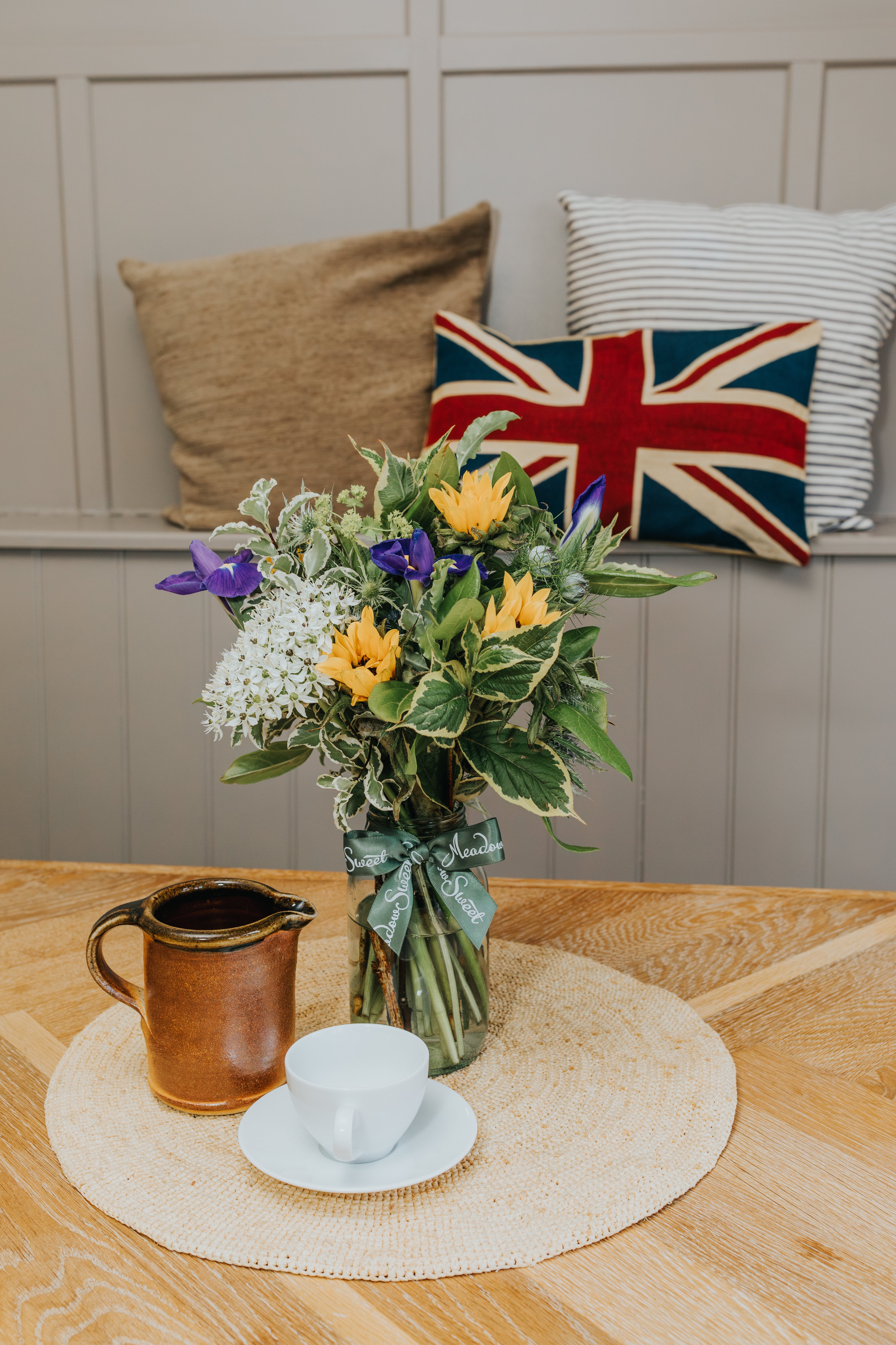 A flower posy of British seasonal flowers and sunflowers and iris in glass jar on wooden table behind Union Jack