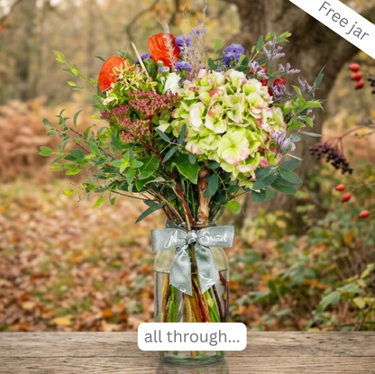 Bouquet of British-grown autumn vibe flowers  and hydrangea in a glass jar in a autumn woodland setting