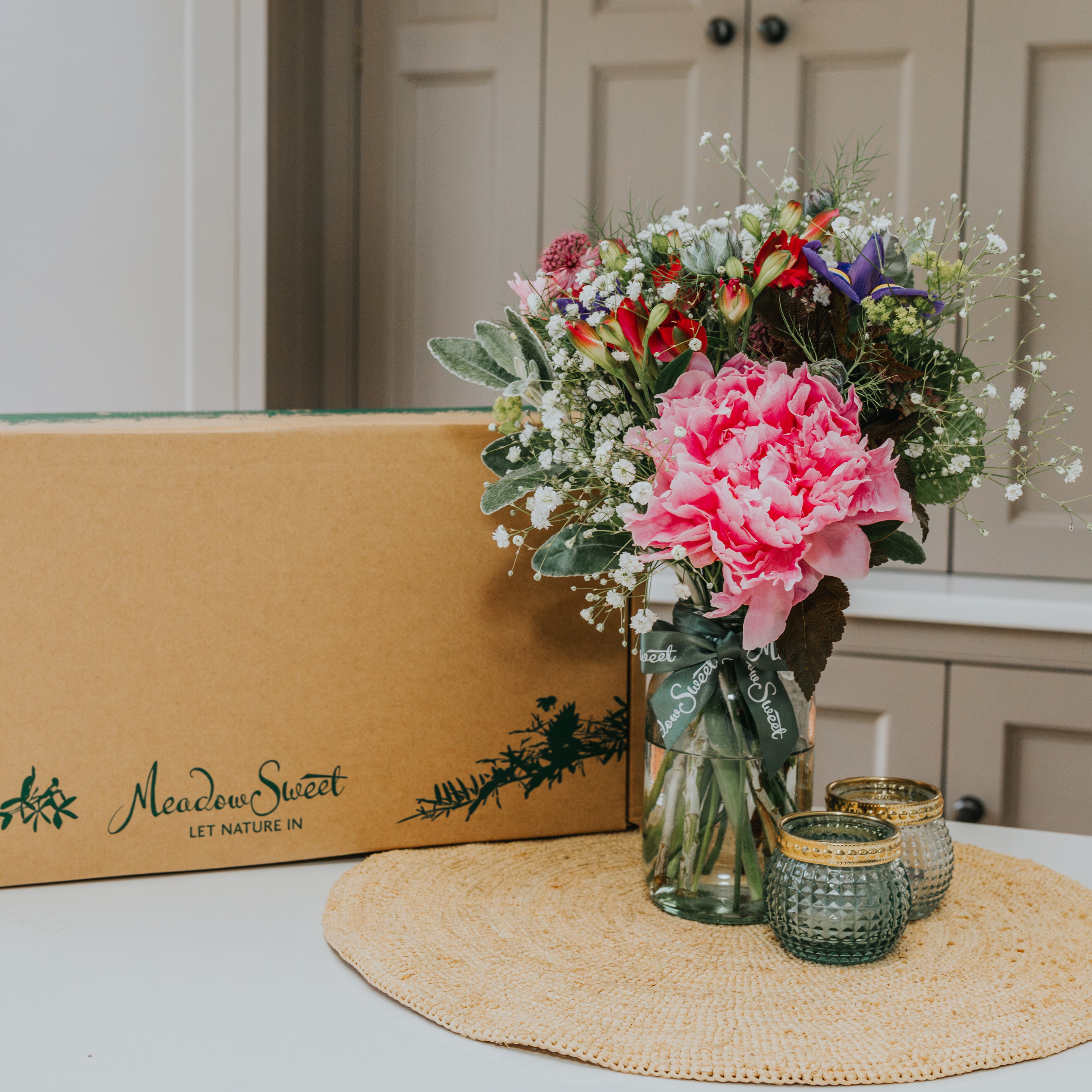 Small Bouquet flower arrangement of MeadowSweet Posies British flowers in glass jar next to UK delivery box
